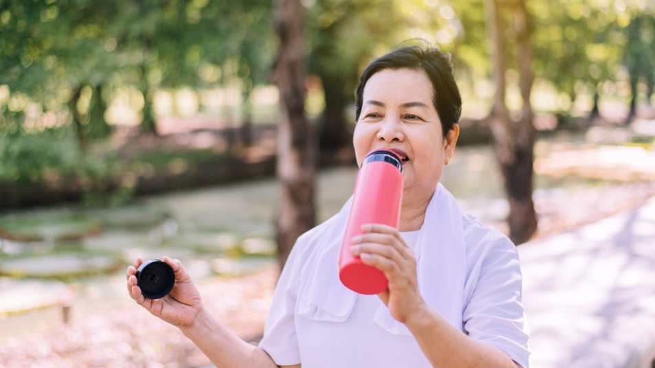 mature woman walking outside drinking electrolyte water out of pink bottle