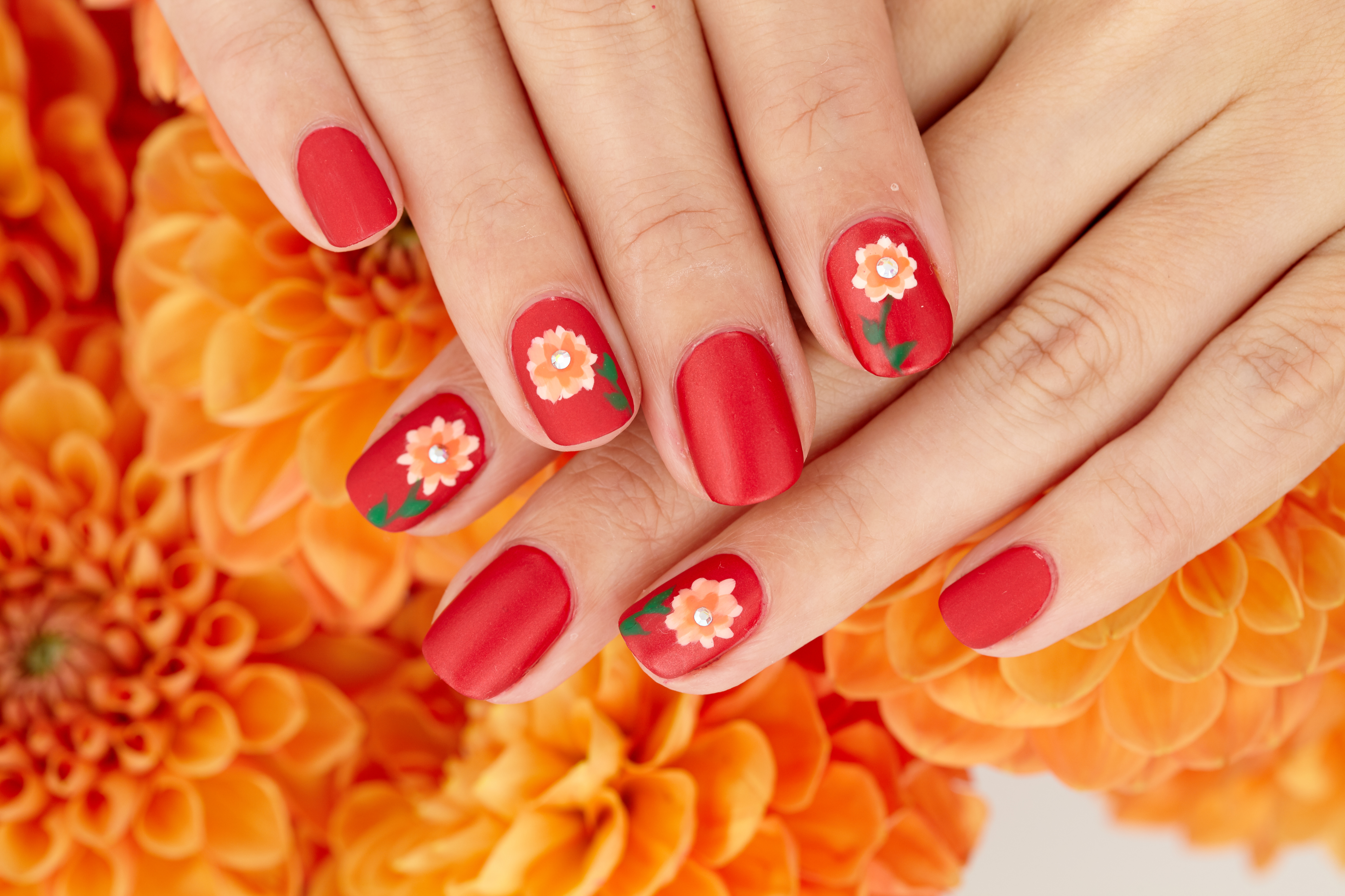 Nails painted red with dahlia fall nail designs on top of a floral background