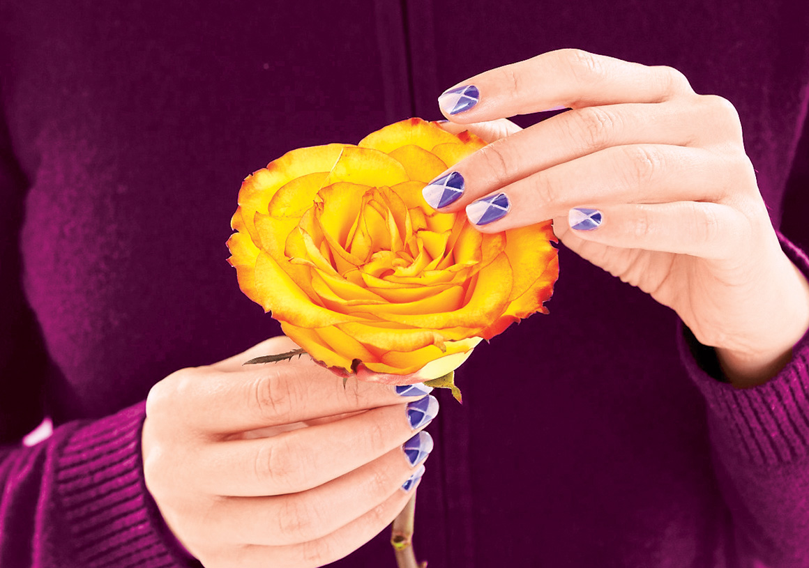A woman holding a rose with her nails painted in a tricolor argyle fall nail designs