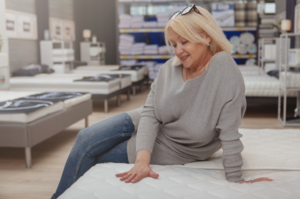 woman sitting on orthopedic mattress at furniture store after learning about fiberglass mattress