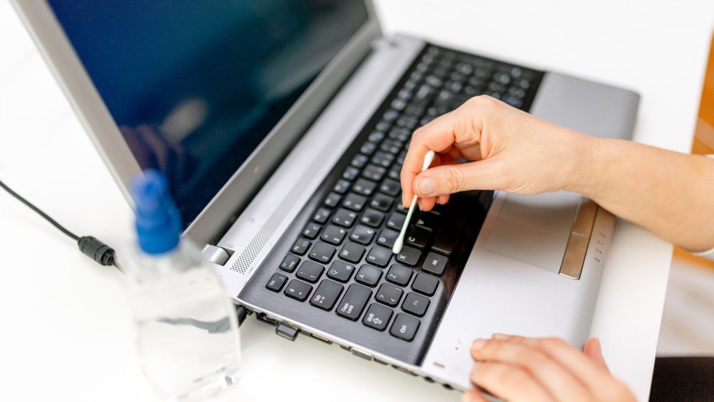 Woman cleaning her computer keyboard with cotton swab