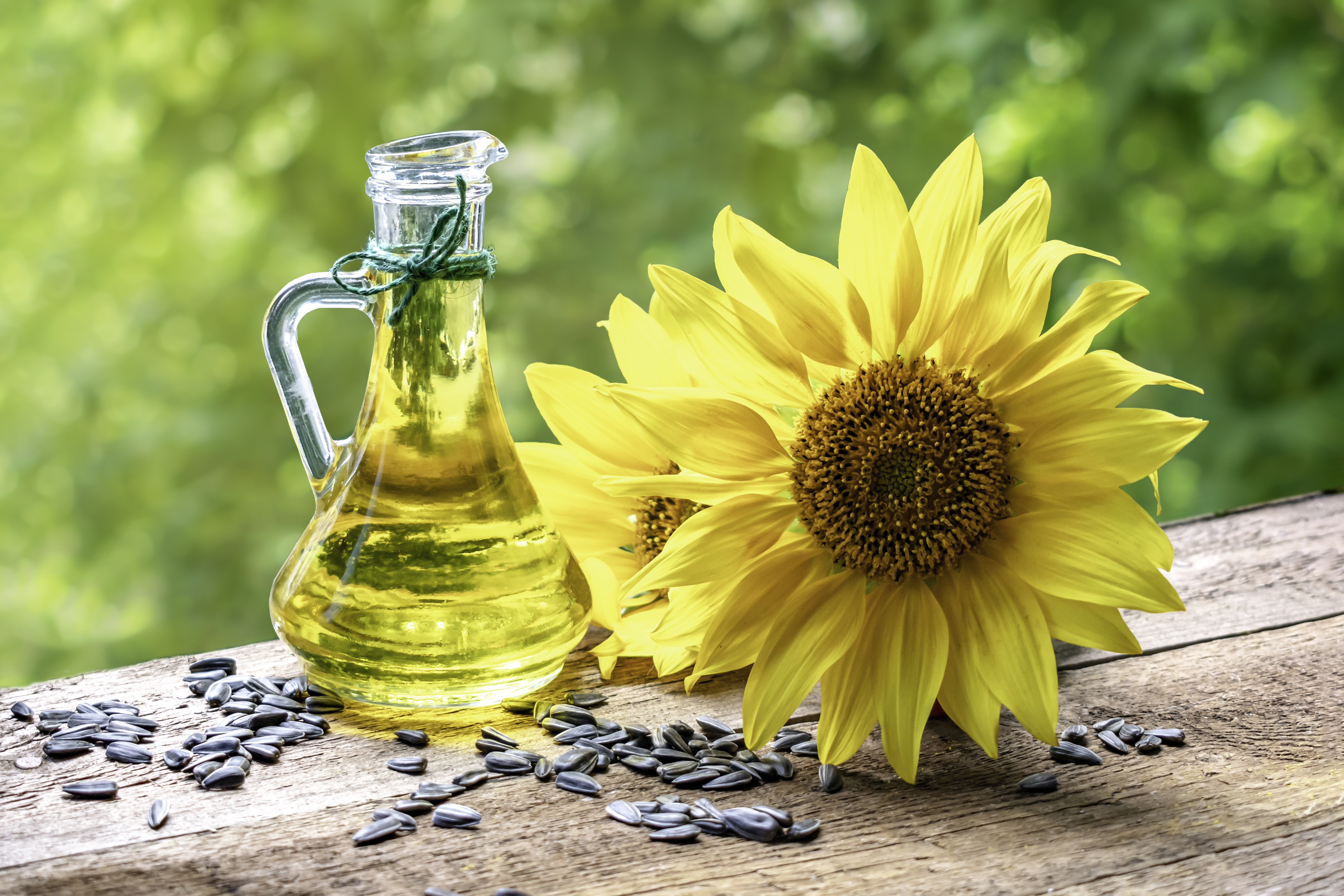 A bottle of sunflower seed oil on a wooden table with a sunflower and sunflower seeds