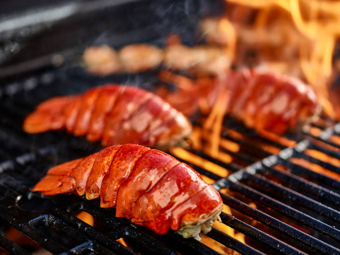 Lobster tails meat-side down on a hot grill with flames