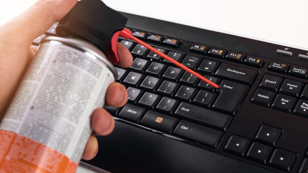 Man cleaning dust from computer keyboard with can of compressed air
