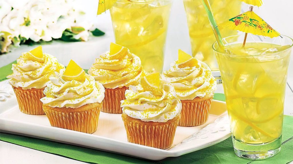 Spiked Lemonade Cupcakes sits on a table next to some lemonade (cocktail cupckaes)