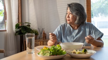 Asian Elderly retired grandmother stay at home with painful face sitting alone on eating table in house. Depressed mature Senior old woman upset feeling unhappy, lonely and missing her family at home