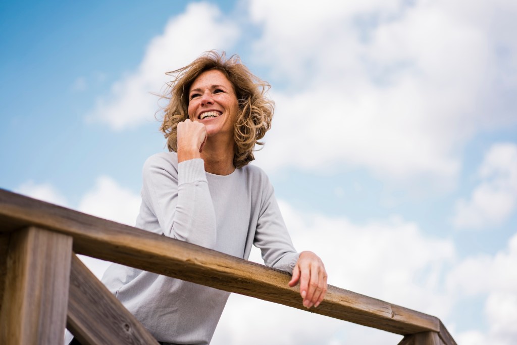Happy mature woman leaning on railing under cloudy sky (orange essential oil benefits.) 