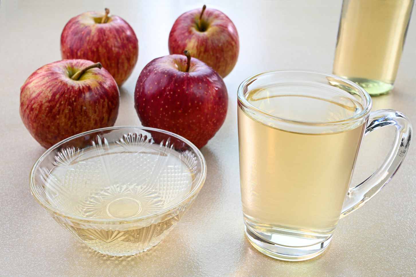 Apple cider vinegar in a glass cup and bowl apples in the background.