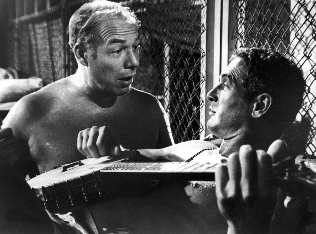 Paul Newman young playing a banjo, and George Kennedy talk in a still from the film 'Cool Hand Luke' directed by Stuart Rosenberg. Newman won a Best Actor Oscar while Kennedy won a Best Supporting Actor Oscar for their roles in the film