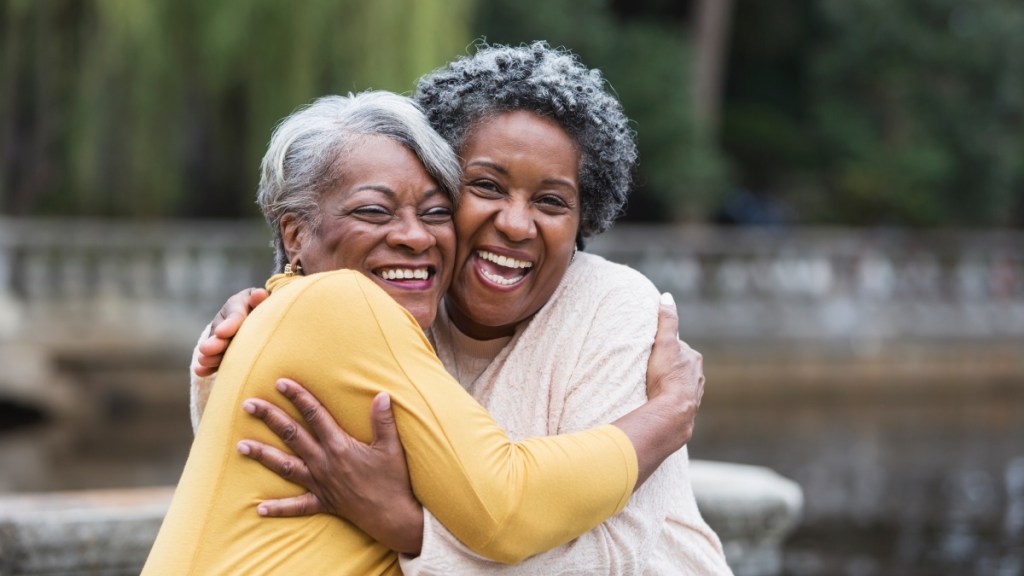 Two African American women with grey hair embracing in a hug and smiling