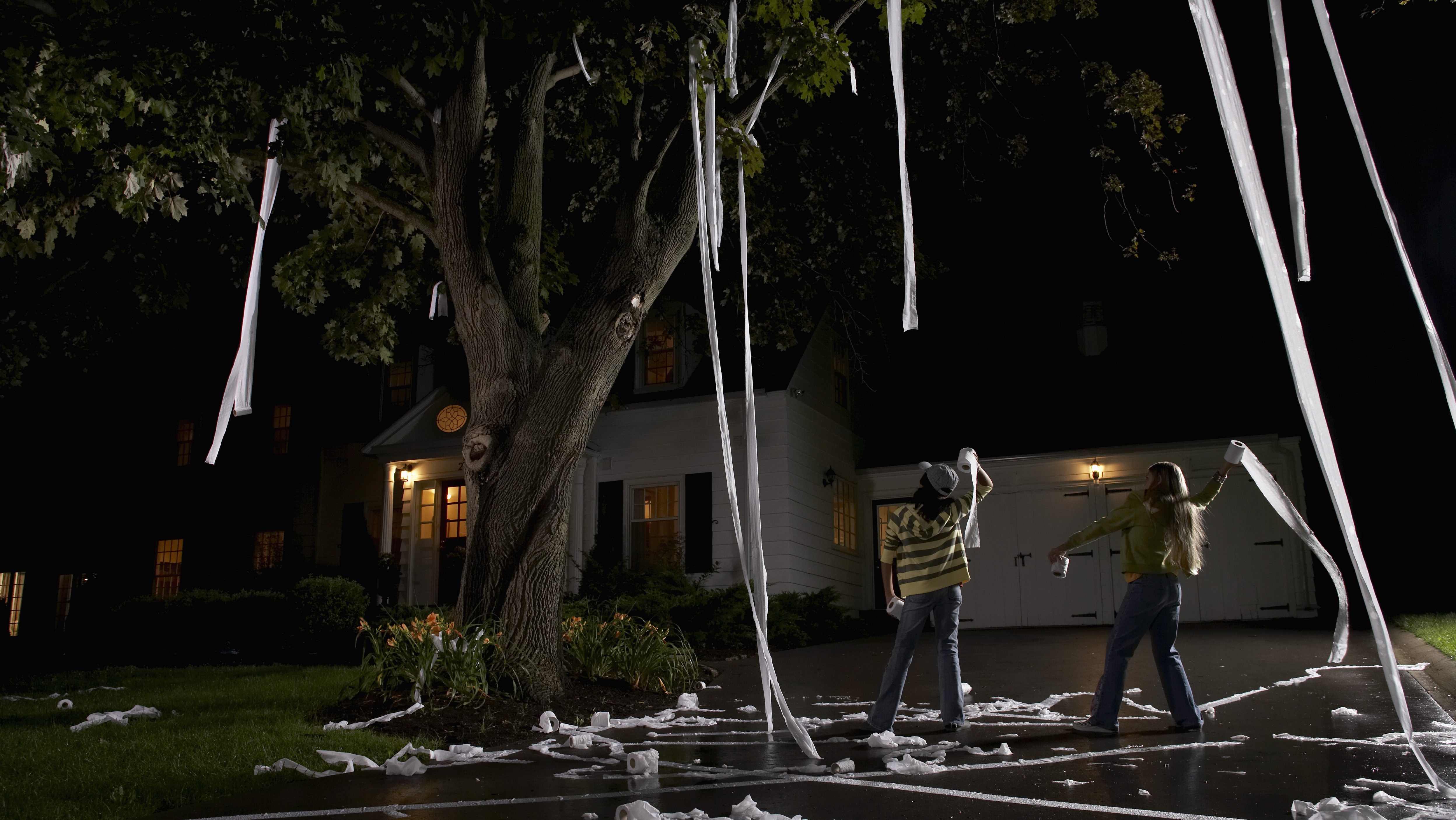 Two girls throwing toilet paper across someone's lawn