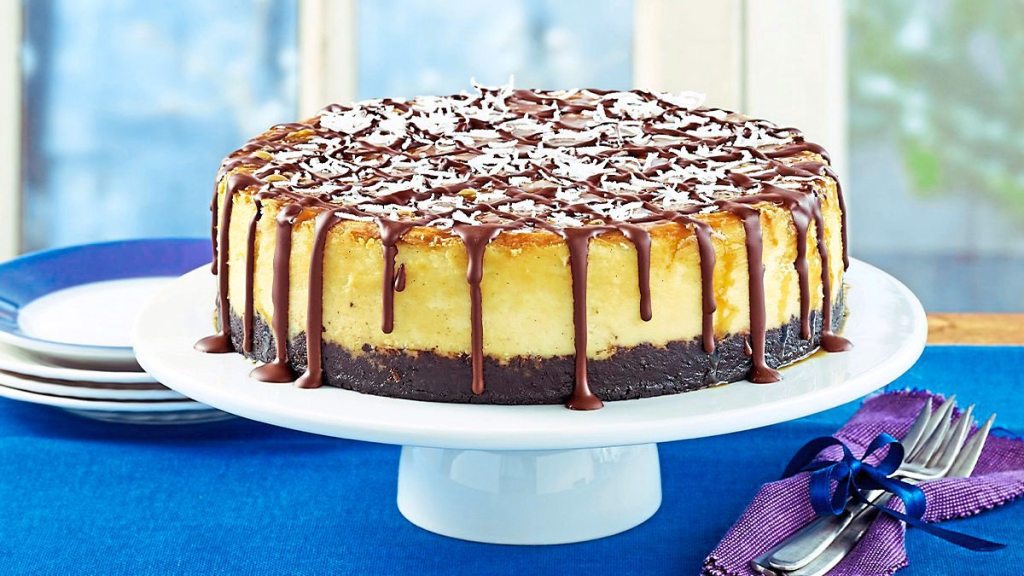Samoa Cheesecake with Fudge Drizzle sits on a blue table (coconut desserts)