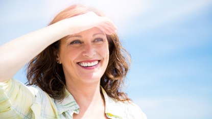 Happy beautiful middle aged woman protecting from sun with hand as a sun visor