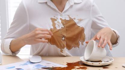 How to clean coffee: Woman in dirty shirt at wooden desk with coffee spill, close up
