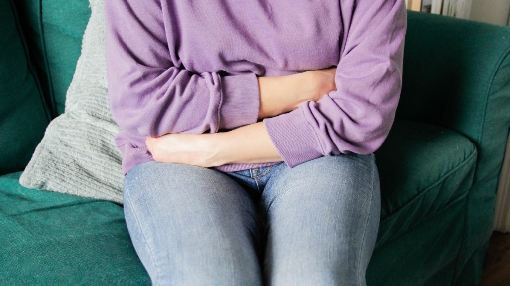 A woman in jeans and a purple top on a green velvet couch who has stress-triggered diarrhea