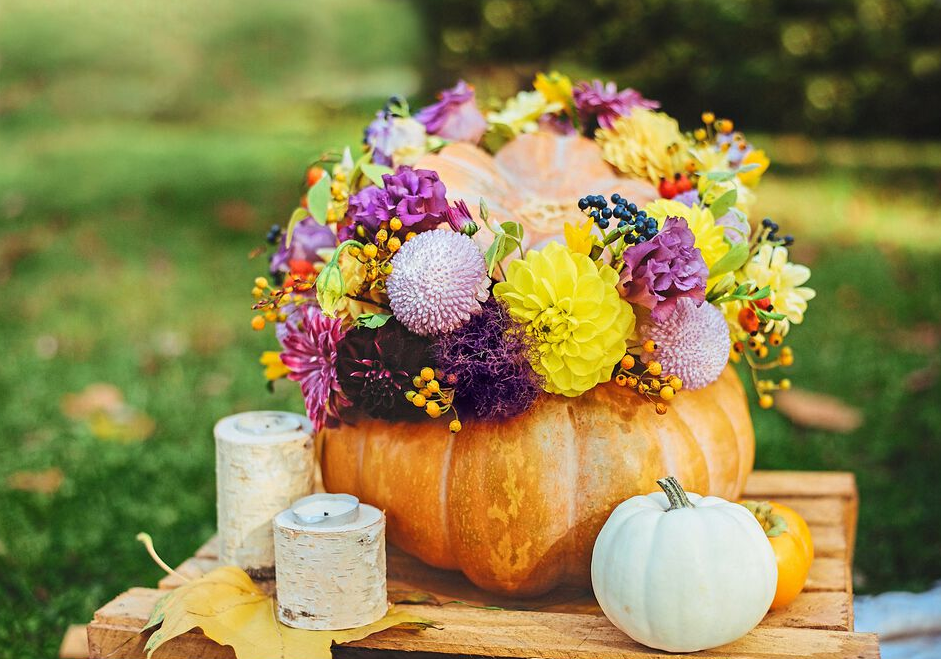 Table centerpiece ideas: Blooming pumpkin (pumpkin filled with fresh fall flowers) shown on outdoor table surrounded by candles