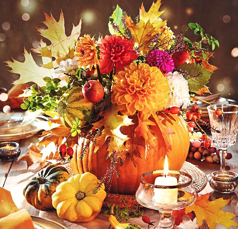 Table centerpiece ideas: Gorgeous autumn blooms brimming from the center of an orange-hued pumpkin placed on a dining table for Thanksgiving 