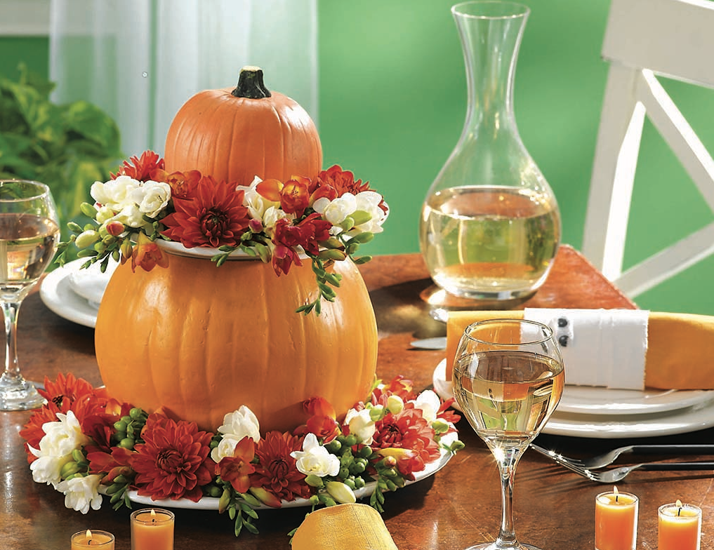 Table centerpiece ideas: Two stacked faux pumpkins adorned with fall flowers and showcased on a Thanksiving table 