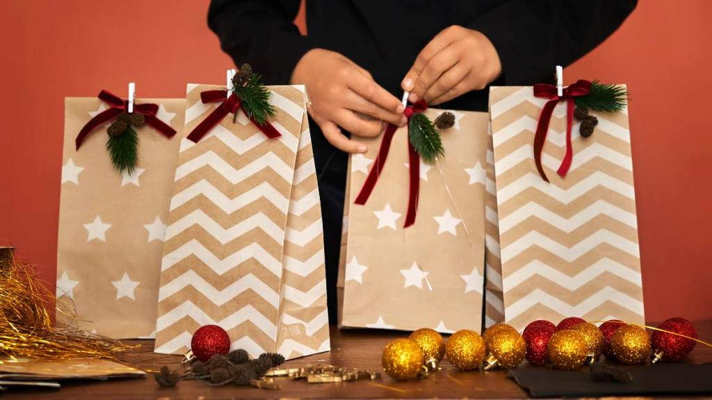 How to wrap a present without tape: Children's hands pack holiday packages with Christmas gifts close-up.