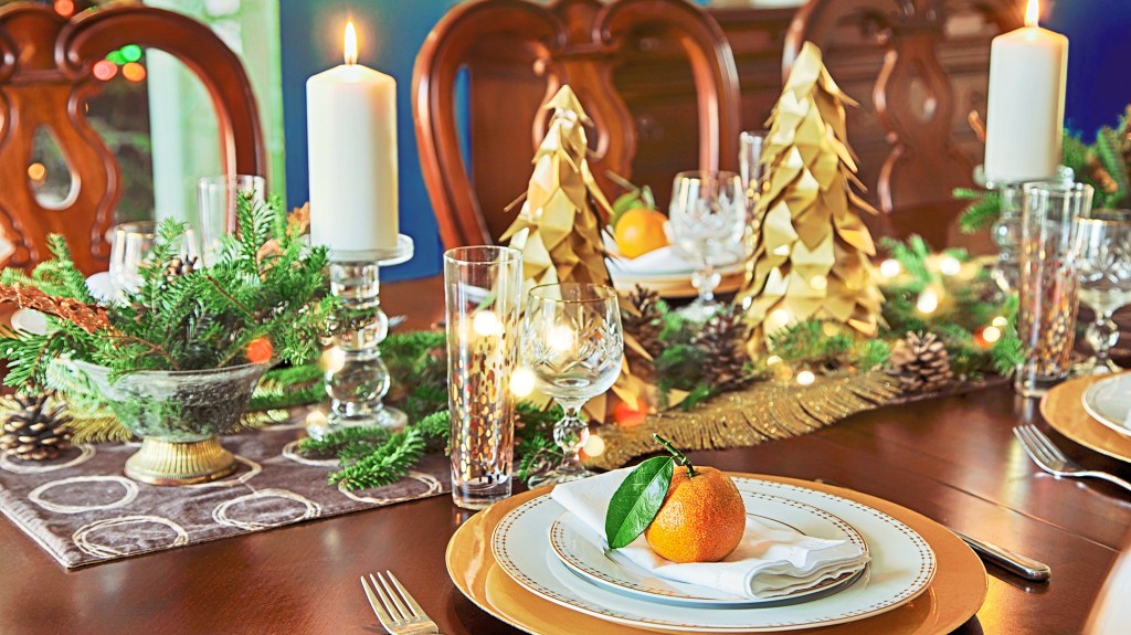 Christmas centerpiece ideas: Dining table decorated with a sparkling centerpiece complete with a gray runner, gold trees, candlesticks, evergreens and pine cones
