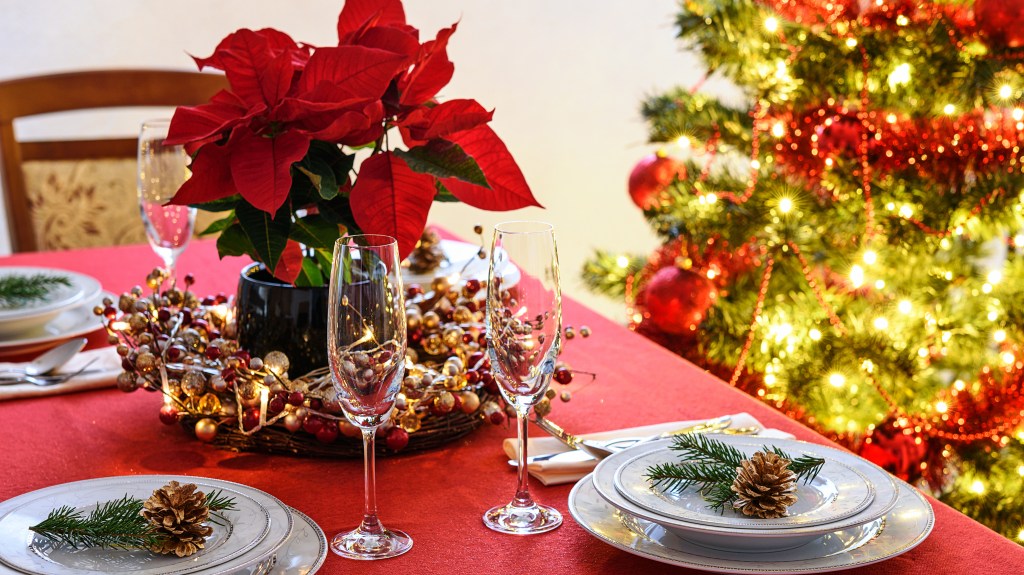 Christmas centerpiece ideas: Festive floral centerpiece on a Christmas dinner table featuring a potted poinsettia nestled into a berry-kissed grapevine wreath
