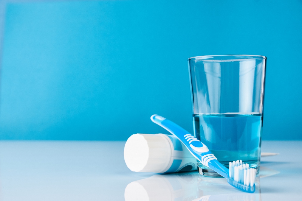 A blue toothbrush with toothpaste and glass of blue mouthwash on blue background with copy space, close-up. Dental oral hygiene concept (How to clean a toothbrush)