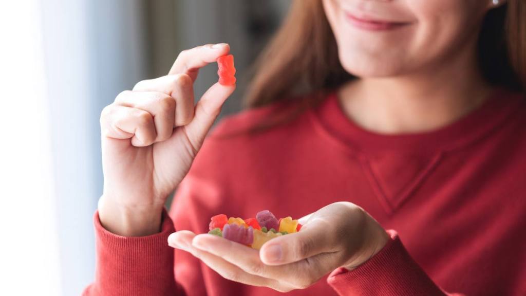 The best foods to eat for gut health: Closeup image of a young woman holding and looking at a red jelly gummy bear