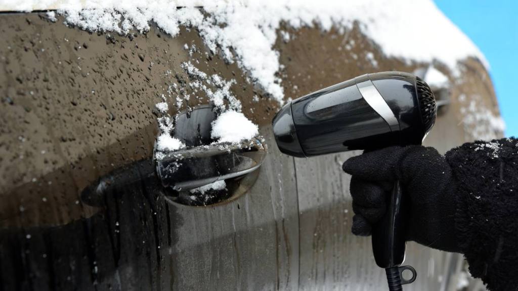 The woman holds a hair dryer in her hand and defrosts the car lock