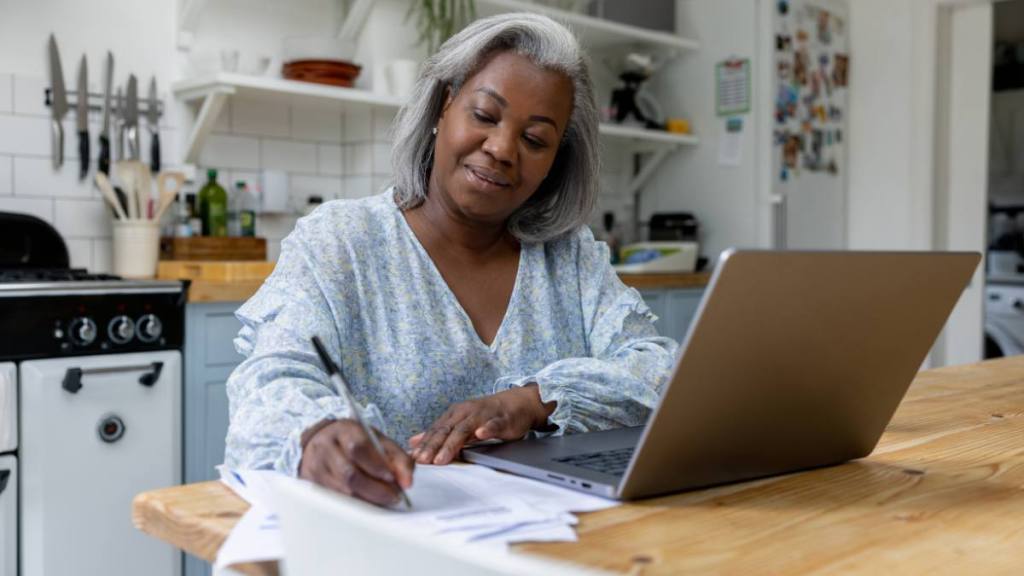 Mature black woman at home  using her laptop and writing some notes