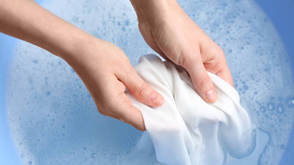 How to remove bleach stains: Top view of woman hand washing white clothing in suds, closeup
