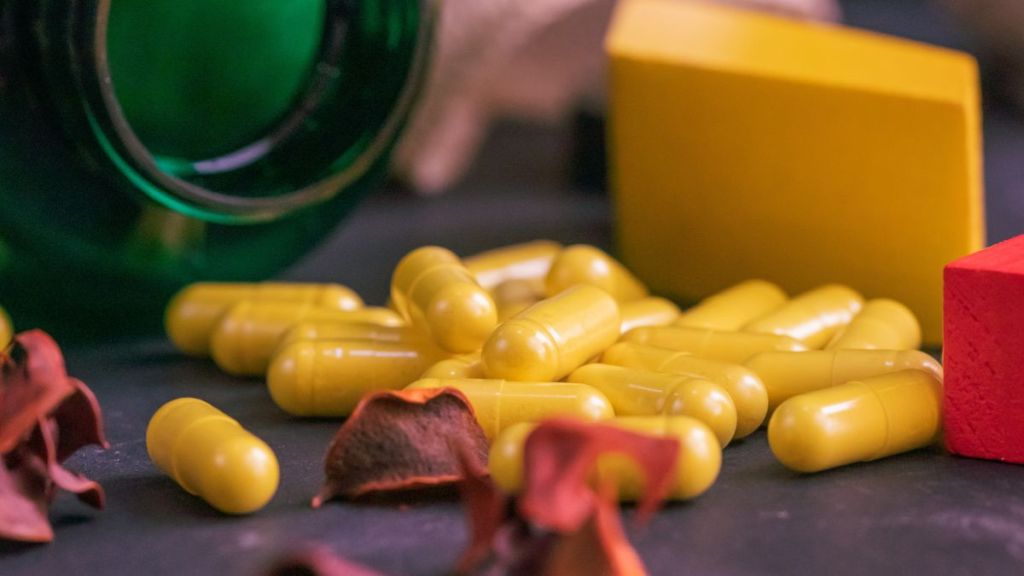 Tiktok health trends: Green bottle of supplements with yellow capsules on a black background.