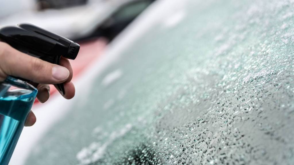 Woman uses a bottle of de-icer to defrost the ice-covered windshield