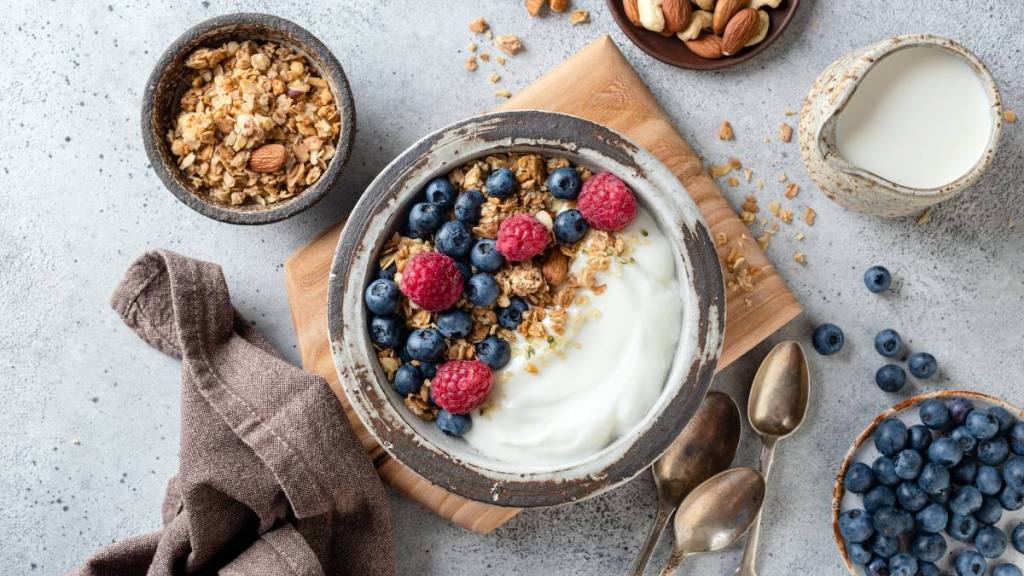 The best foods to eat for gut health: Yogurt granola bowl with blueberries and raspberries on wooden board, table top view. Healthy vegetarian food