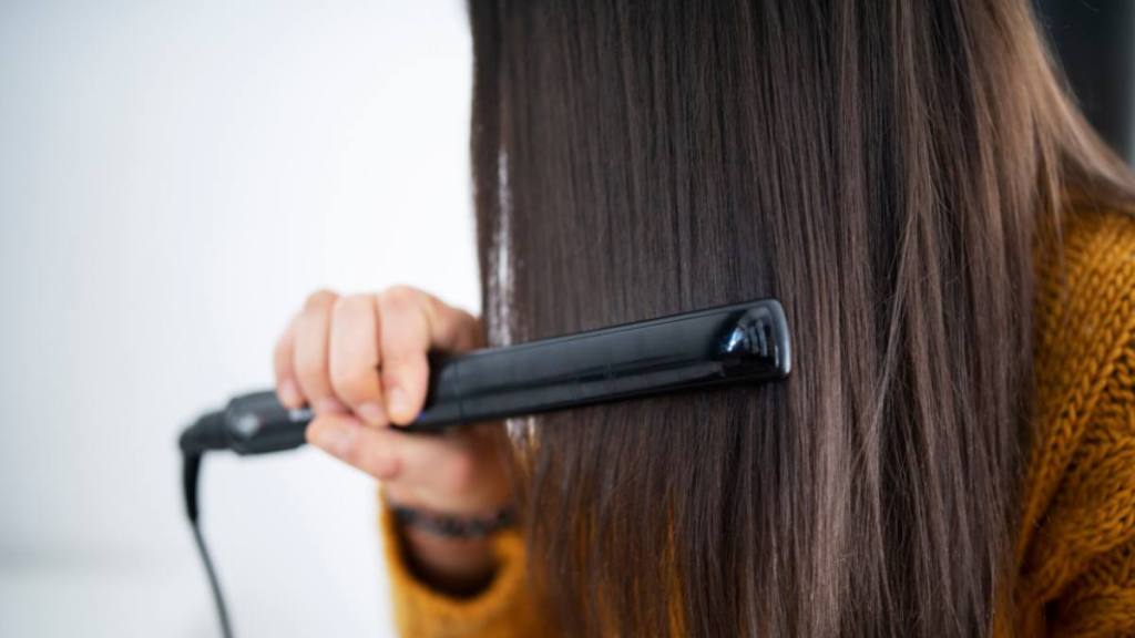 how to clean a flat iron: Unrecognizable woman using hair straightener.