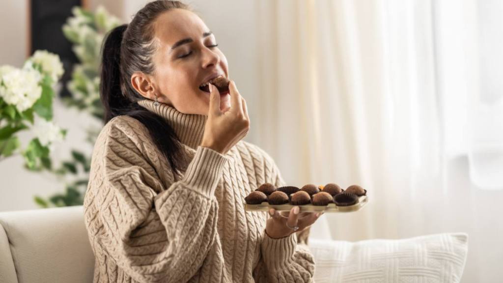 period diarrhea: A young woman couldn't resist the sweet temptation to eat chocolate candies and enjoys them with her eyes closed.