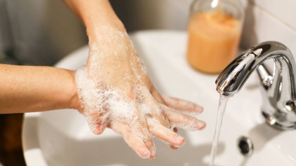 How to prevent food poisoning: Washing hands. Hands washing with proper technique and antibacterial soap on background of flowing water in bathroom. Rubbing fingers. Prevent coronavirus epidemic. Prevention of flu disease.