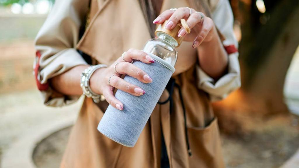 how to clean reusable water bottle: Woman holding reusable glass bottle
