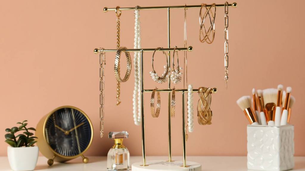 How to Untangle a Necklace: Holder with set of luxurious jewelry on dressing table near pale pink wall