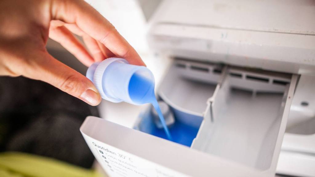 A close-up of a woman pouring blue laundry detergent into a washer