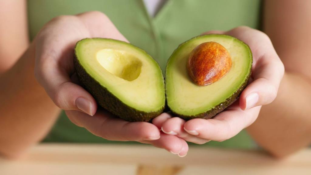 refined sugar: Woman holding halved avocado