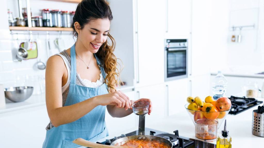 How to prevent food poisoning: Young woman adding pepper and mixing food in frying pan