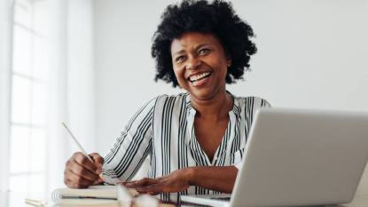Marriott work from home jobs: Portrait of a smiling woman sitting at table with laptop and dairy. Woman smiling at camera while working from home office.