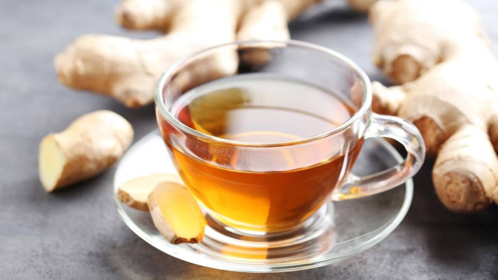 Cup of tea, which can help with bloating, with ginger root on grey wooden table