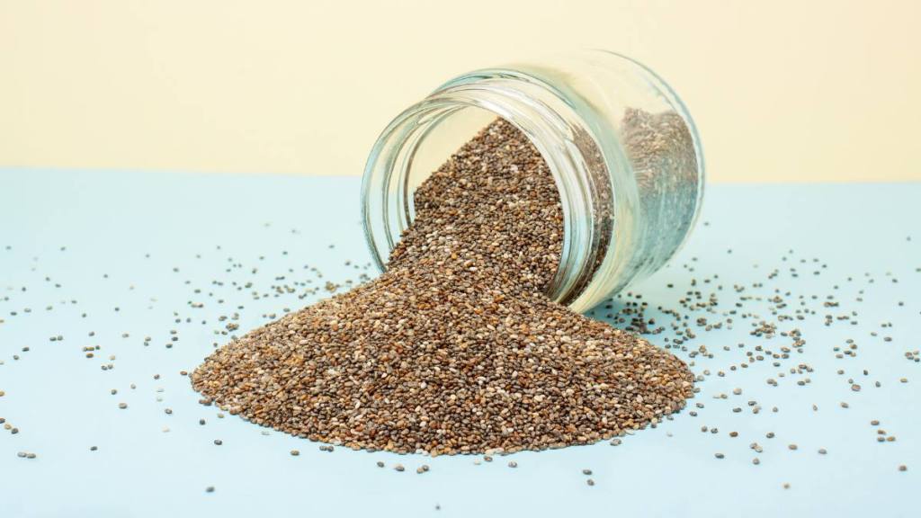 refined sugar: Chia seeds spilling out of a glass jar on a blue-yellow background. Healthy food concept, superfood, dietary supplements.