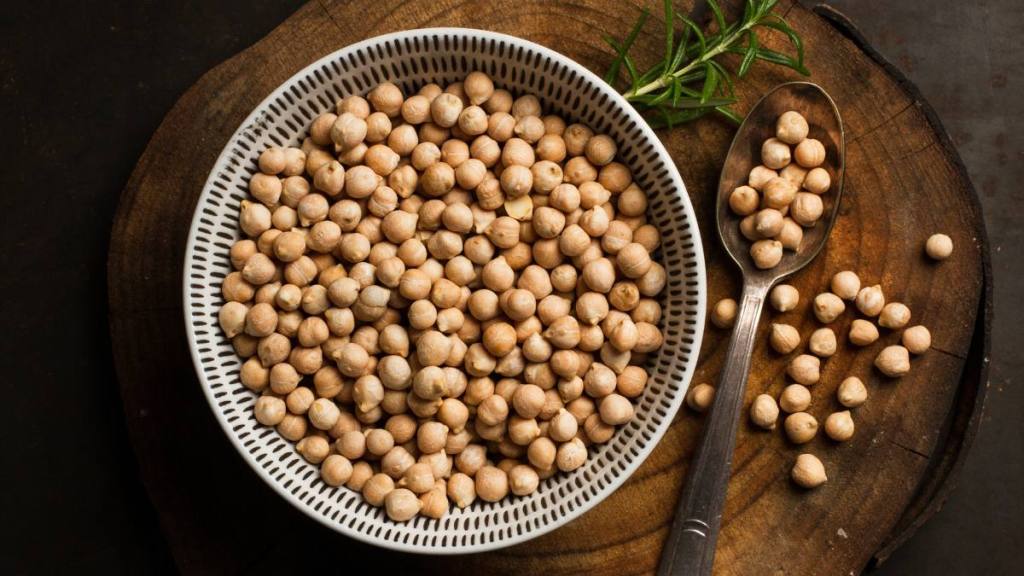 refined sugar: Raw chickpeas in a ceramic bowl on a wooden kitchen board on a black bachground