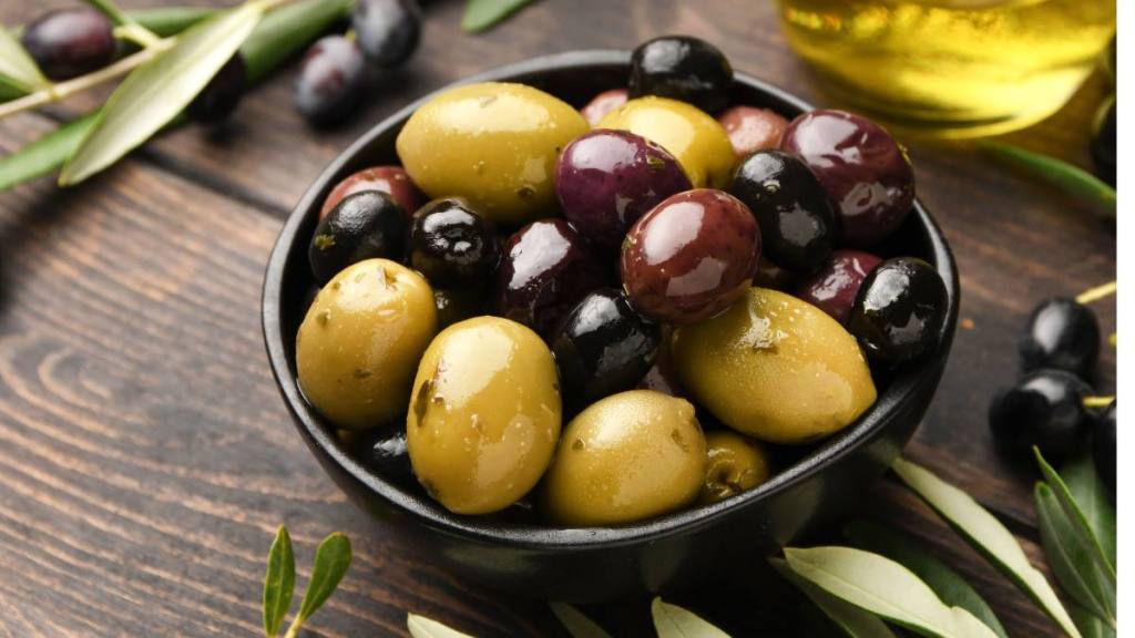 refined sugar: Different kinds of olives in olive oil with herbs on a wooden background with olive tree branches