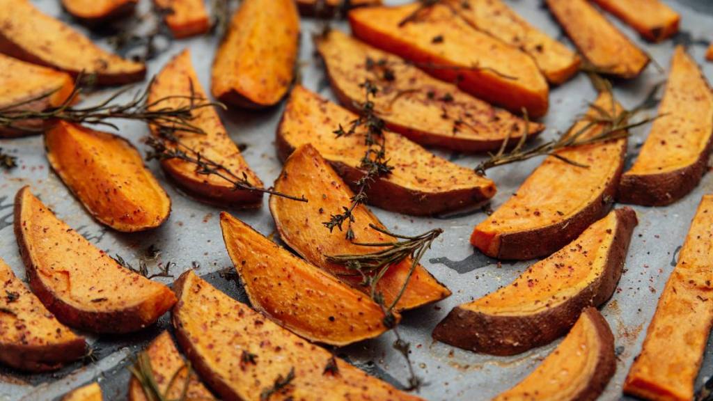 refined sugar: tray of oven baked sweet potato chips in closeup. Baked with paprika, rosemary and salt. Homemade cooked sweet potatoes with spices and herbs on oven-tray.