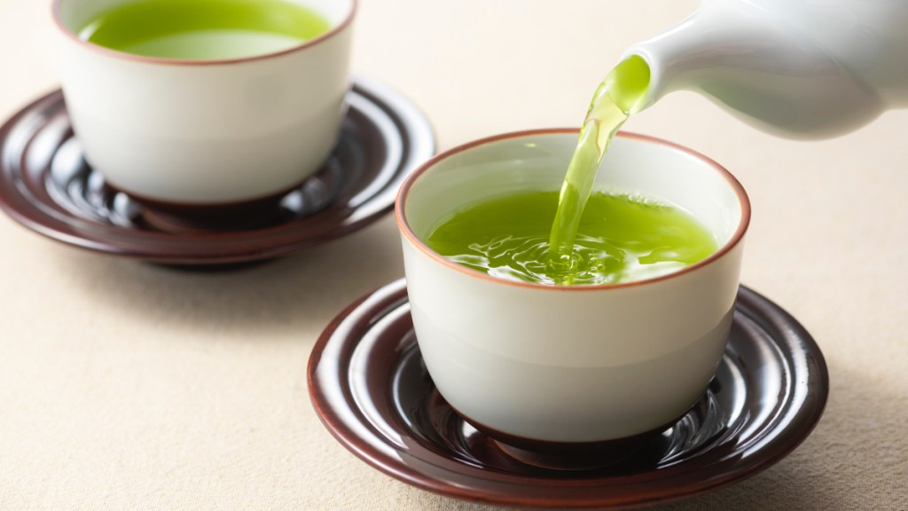 Two cups of green tea, one of the best cortisol-lowering foods, with a teapot pouring fresh tea
