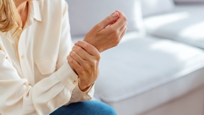 A woman in a white shirt holding her wrist, which can benefit from carpal tunnel syndrome self-care