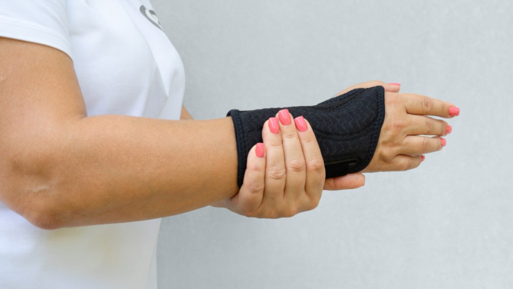 A woman in a white shirt with pink nails wearing a black wrist splint for carpal tunnel syndrome